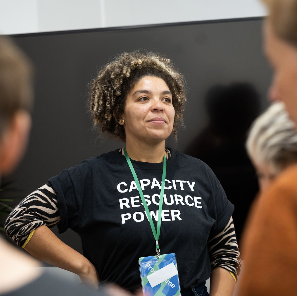 The image is of a brown-skinned women with black and blonde curly hair wearing a black t-shirt with the phrase 'Capacity, Resource, Power' on it.
